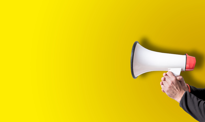 holding megaphone with both hands against yellow background